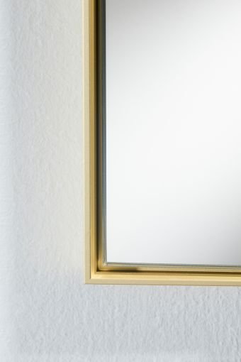 Close-up of Lucka Gold Rect., showing matte gold aluminium frame on the rectangular wall mirror.